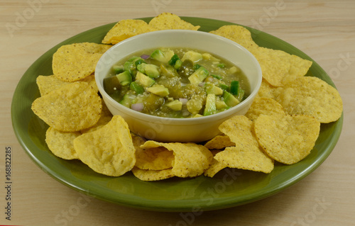 Avocado and tomatillo salsa verde guacamole mixture with round tortillas chips on green plate