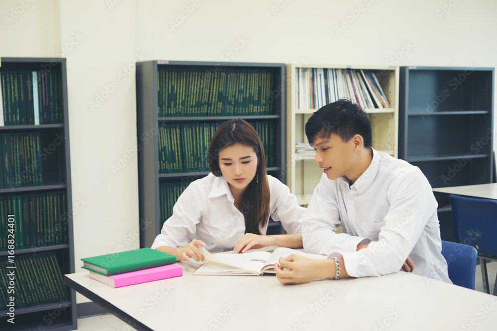 Young Asian Couple of students at the library reading a book together. Education concept. Young Asian Couple of students at the library reading a book together. Education concept.