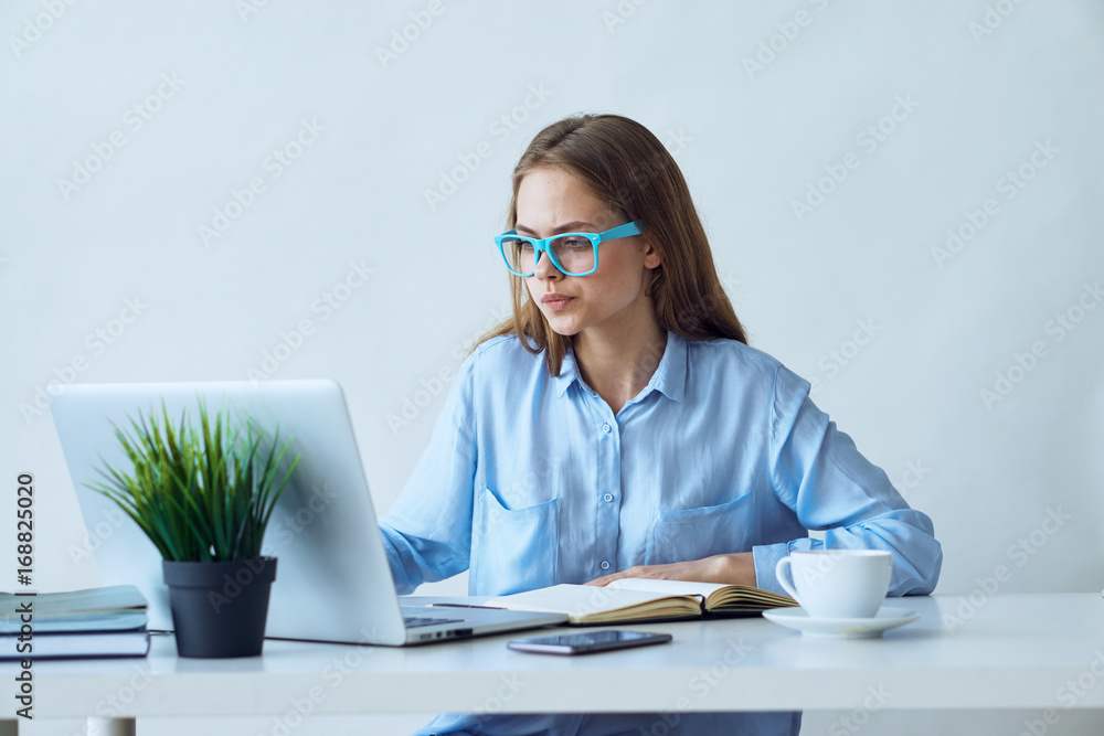Young beautiful woman in glasses works at computer in office