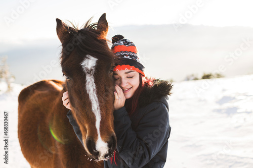 Happy girl gently stroking horse in shiny sunlight. Winter in mountains