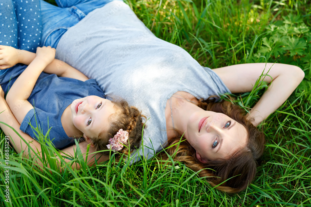 Beautiful young mother and little daughter lying on green grass and resting Beautiful young mother and little daughter lying on green grass and resting