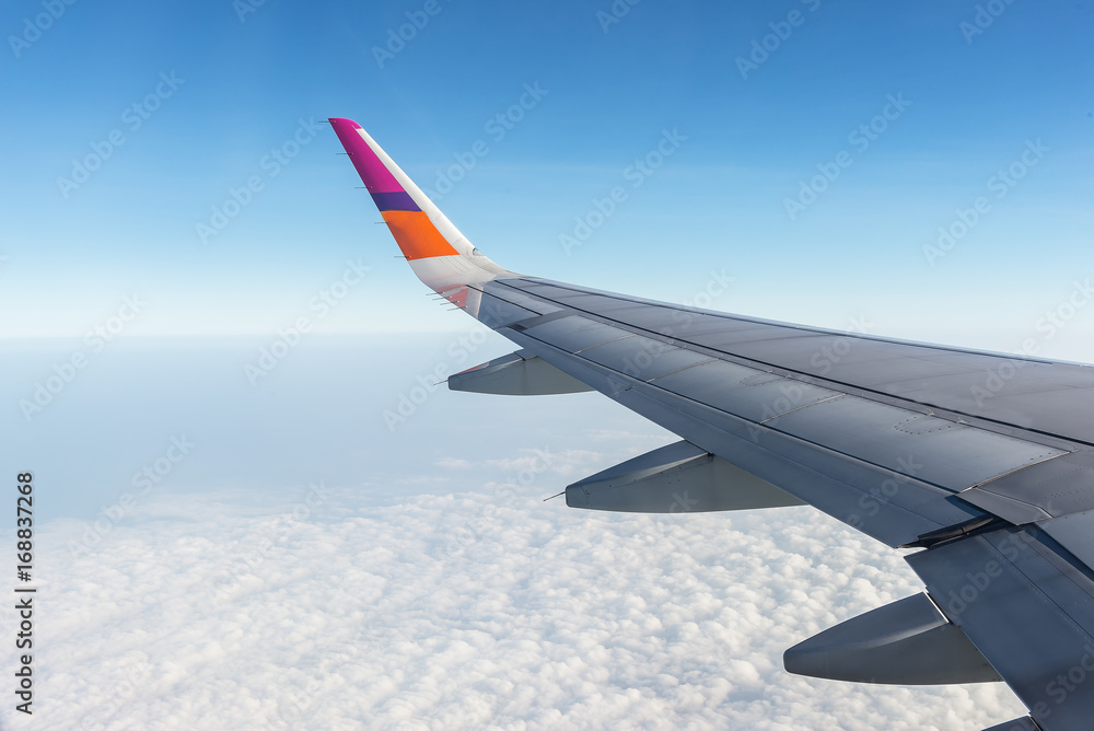 Fototapeta premium Wing of airplane flying above the clouds in the sky, looking through window