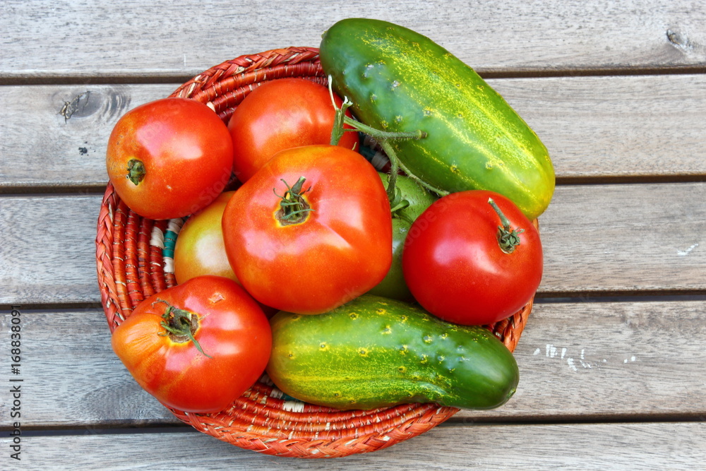 Red ripe Tomatoes and cucumber in a basket on a wooden background