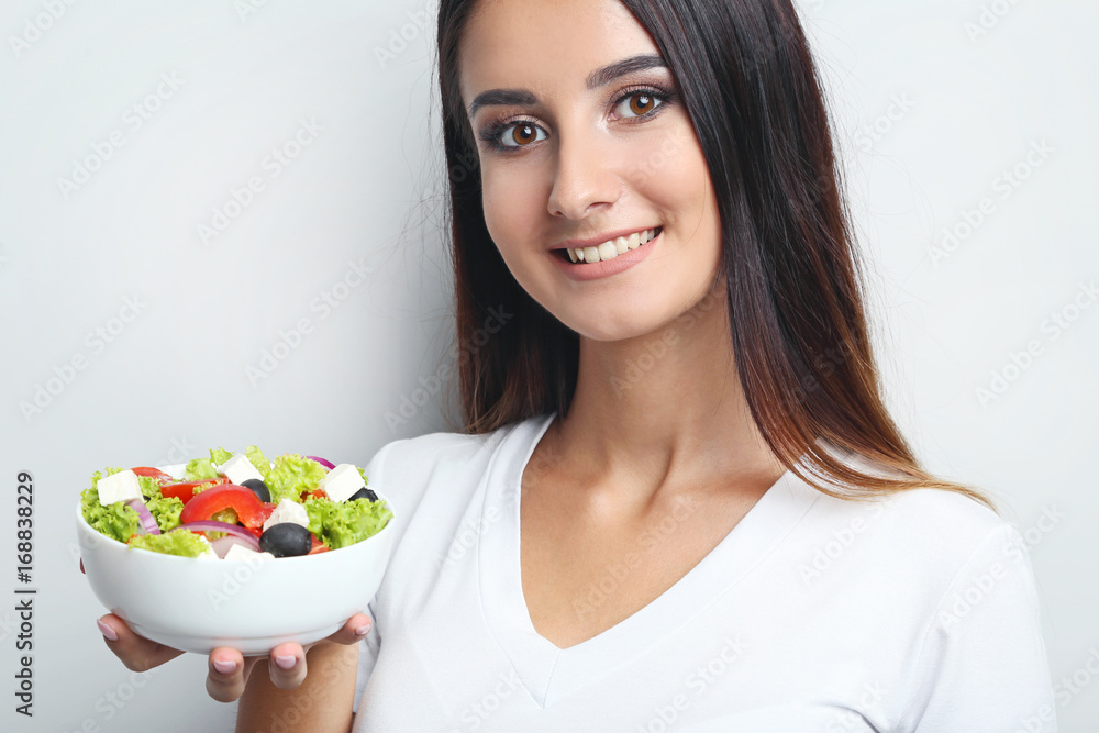 Young woman with vegetable salad in bowl on grey background Young woman with vegetable salad in bowl on grey background