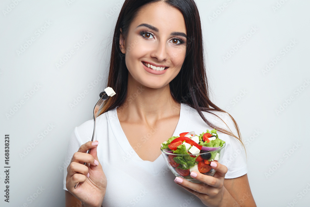 Young woman with vegetable salad in glass bowl on grey background Young woman with vegetable salad in glass bowl on grey background