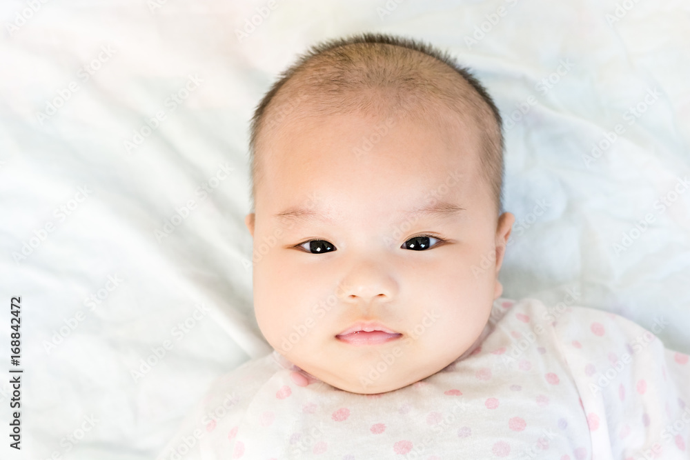 Portrait of adorable baby girl lying on back on the bed and looking in camera indoors Portrait of adorable baby girl lying on back on the bed and looking in camera indoors
