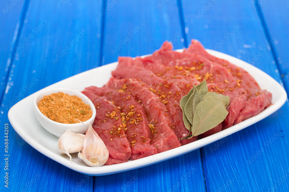 raw meat with herbs on white dish on blue wooden background raw meat with herbs on white dish on blue wooden background