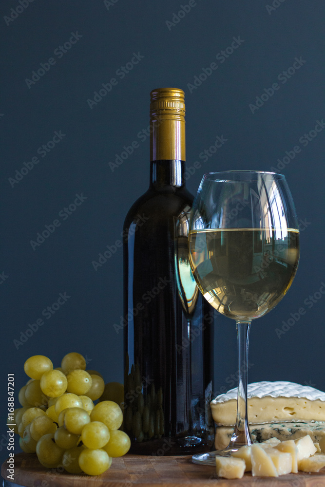 Fototapeta premium Bottle and glass with white wine near cheese composition on a wooden board