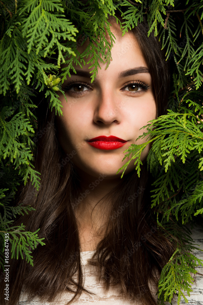 Beautiful woman with red lips posing on a background of thuja Beautiful woman with red lips posing on a background of thuja