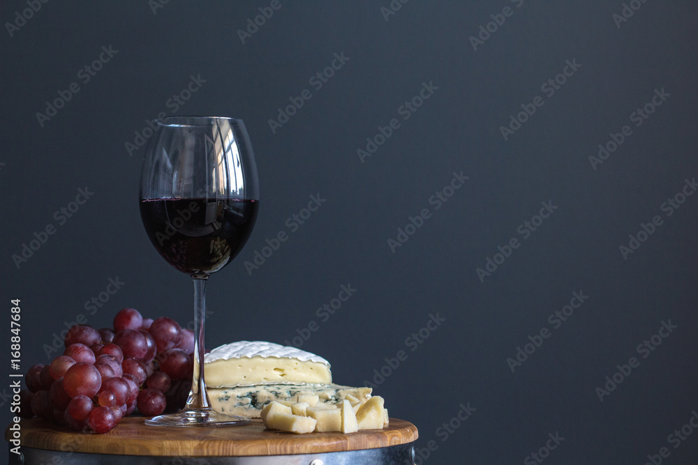 Glass with red wine and grapes near cheese composition