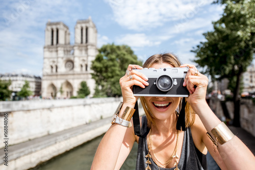 Young woman tourist photographing with camera standing in front of the famous Notre Dame cathedral in Paris