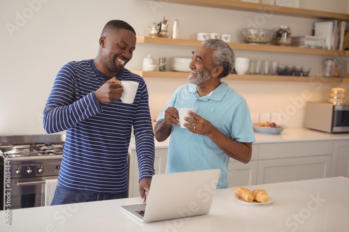 Father and son using laptop while having coffee in kitchen