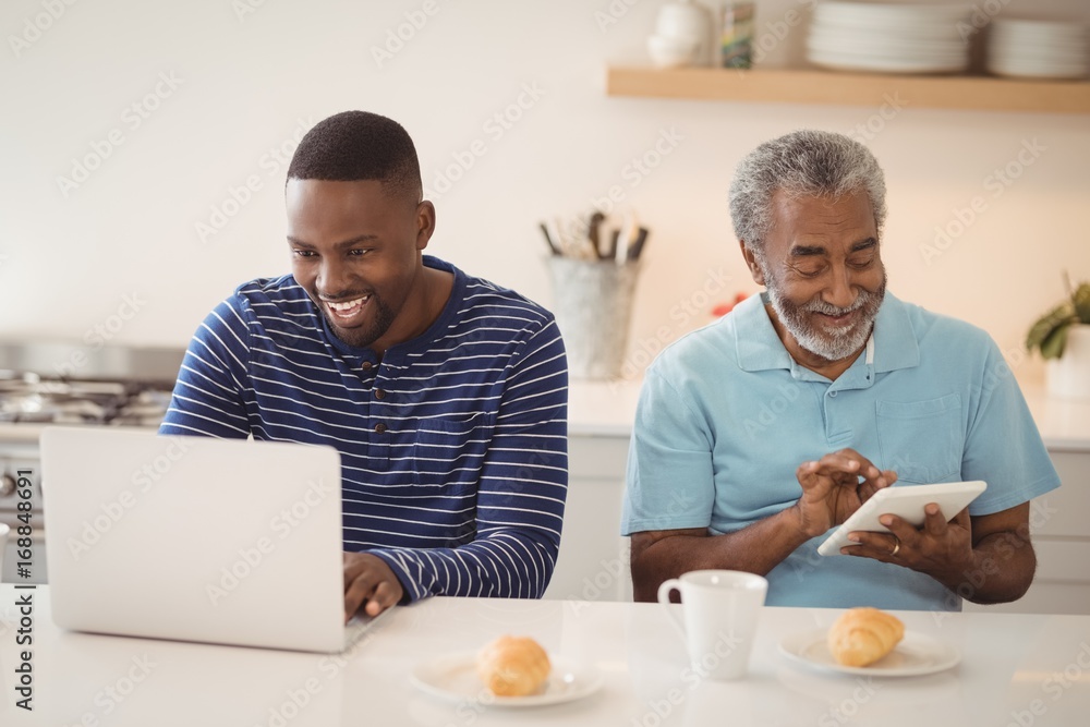 Father and son using laptop and digital tablet in kitchen Father and son using laptop and digital tablet in kitchen