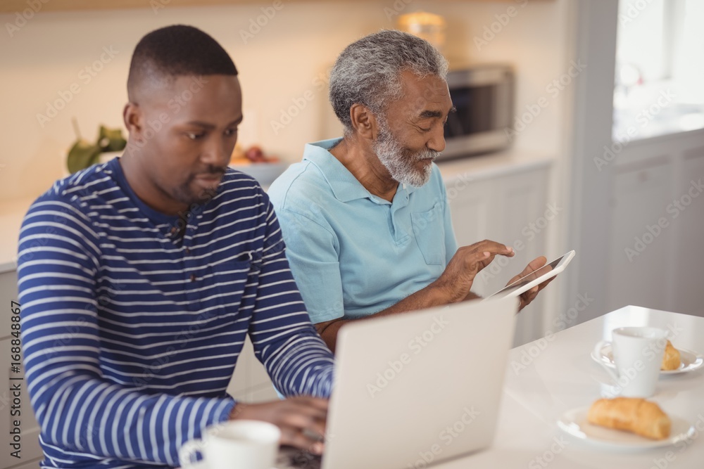 Father and son using laptop and digital tablet in kitchen Father and son using laptop and digital tablet in kitchen