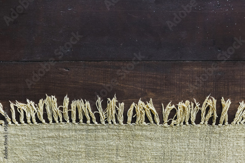 Beige carpet with fringe on dark wooden floor, texture close up photo