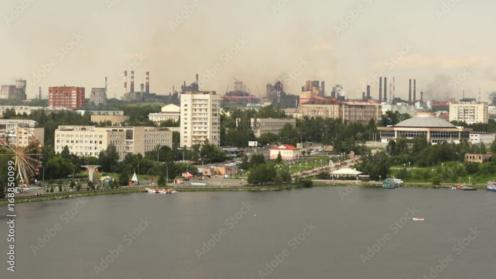 Time-lapse of heavy industry plant in the city. Quay with amusement park, city landscape against the background of smoke from the pipes of the metallurgical plant, atmospheric pollution. Time-lapse of heavy industry plant in the city. Quay with amusement park, city landscape against the background of smoke from the pipes of the metallurgical plant, atmospheric pollution.