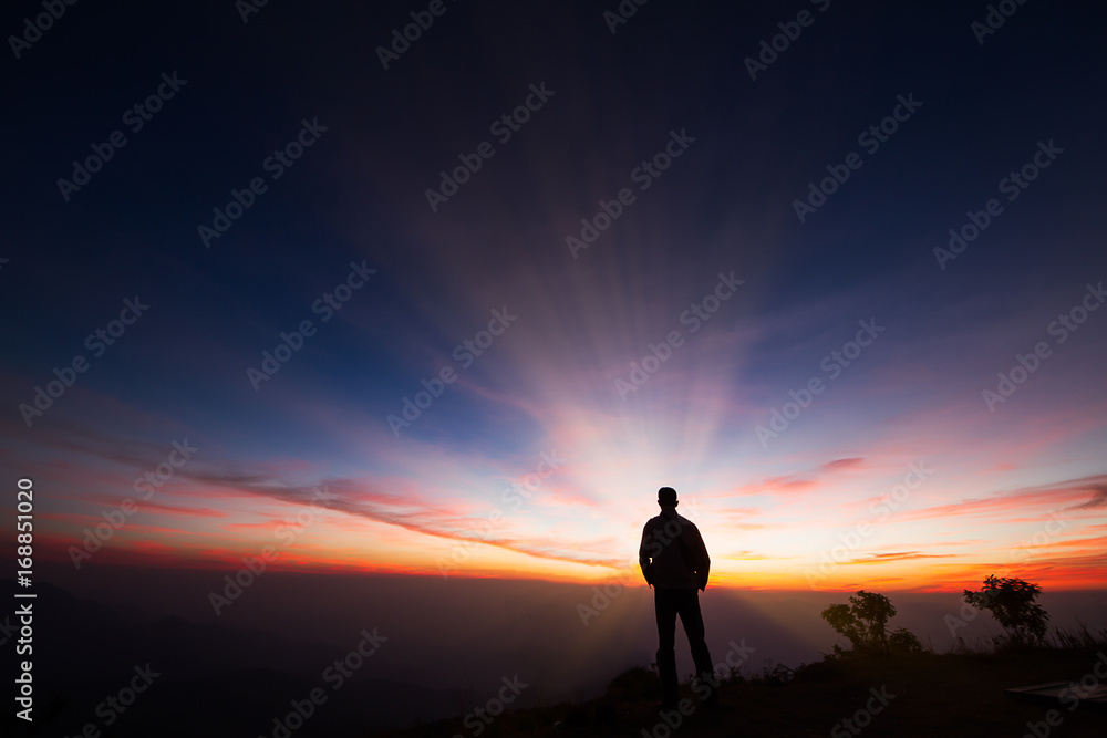 Silhouette of a man standing on the cliff looking at sunrise background, hope and following a dream concept Silhouette of a man standing on the cliff looking at sunrise background, hope and following a dream concept