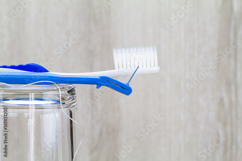 Interdental brush, toothbrush and dental floss on clean glass on blurred wooden background in bathroom