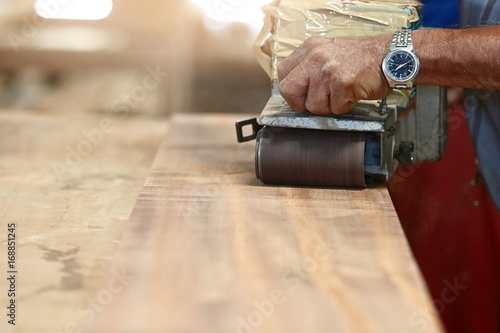 Front view of belt sander working on a piece wood with hands of worker with copy space. Selective focus and shallow depth of field.
