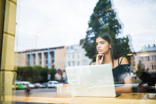 Woman working on a computer at a cafe while look through the window glass.