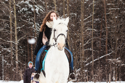 Girl, horse trainer and white horse in a winter