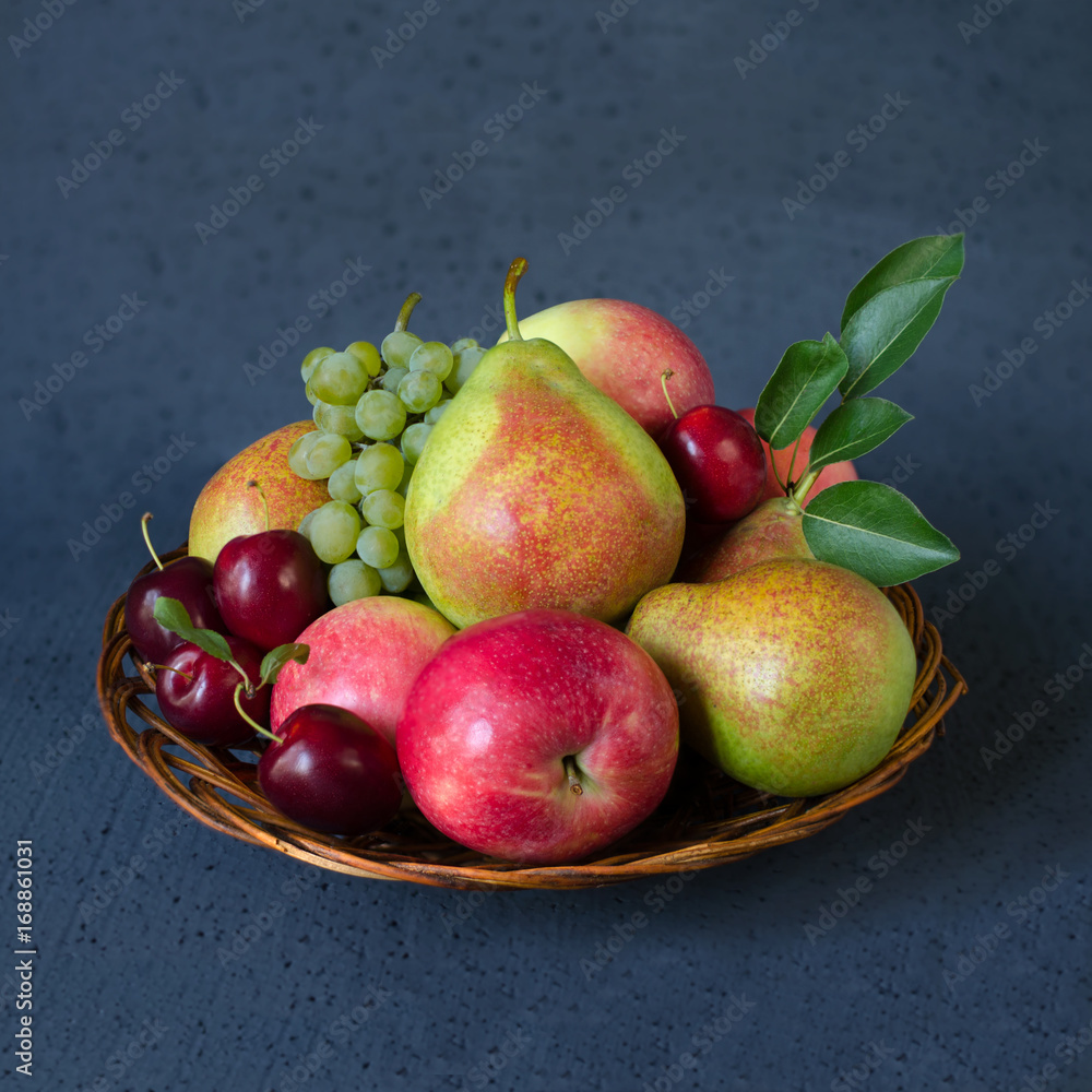 Autumn fruit mix - fresh apples, pears, grapes and plums in a wicker wooden plate. Dark blue background. Harvest concept Autumn fruit mix - fresh apples, pears, grapes and plums in a wicker wooden plate. Dark blue background. Harvest concept
