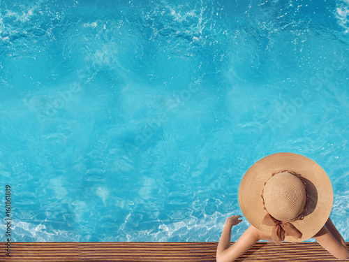 Top view of woman in straw hat relaxing in swimming pool at luxury villa resort. Summer holiday idyllic background. Vacations Concept. Exotic Paradise.