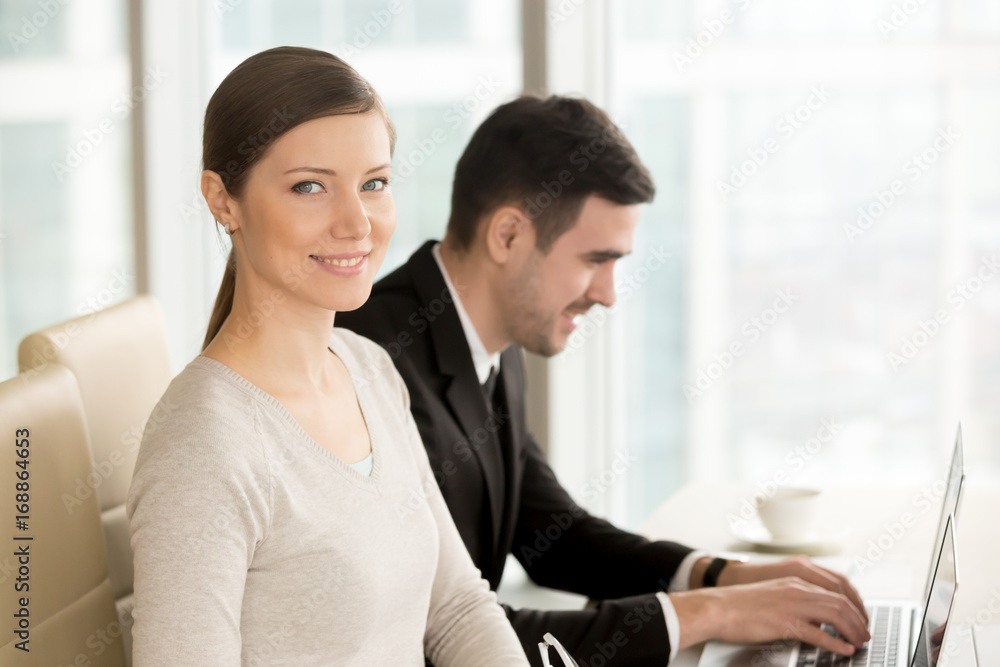 Beautiful smiling businesswoman built successful career posing at workplace with laptop near colleague, ambitious lady looking at camera in office, powerful women in business leadership, portrait Beautiful smiling businesswoman built successful career posing at workplace with laptop near colleague, ambitious lady looking at camera in office, powerful women in business leadership, portrait