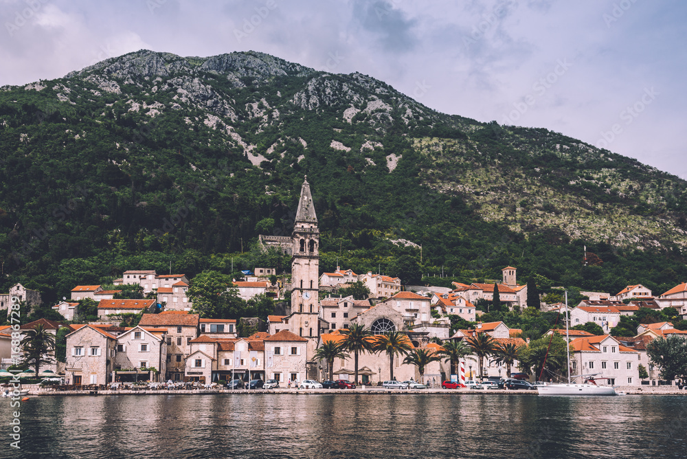 Perast, Montenegro - June 3th, 2016. View to famous coast village Perast Old Town roofs, promenade and mountains from water of Boka Kotorska. Postcard montenegrin landscape.