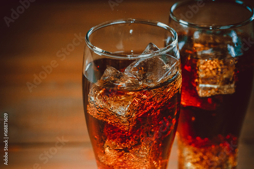 Beautiful cold fizzy cola soda with cubes ice in glasses goblet on old wooden background with free space. Shallow DOF.