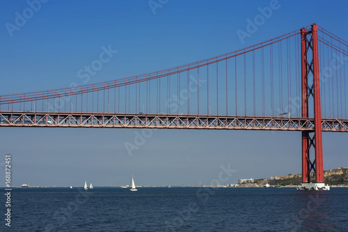 Beautiful view of the red bridge, Ponte 25 de Abril in Lisbon. The bridge connects two cities across the river. Concept of architecture, construction, transportation