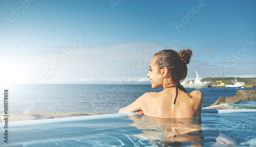 Young cheerful girl swimming in water of pool looking at the water on background of sea  Iceland  West Fjords. back view