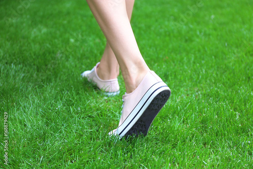 Female legs in pink sneakers on green grass