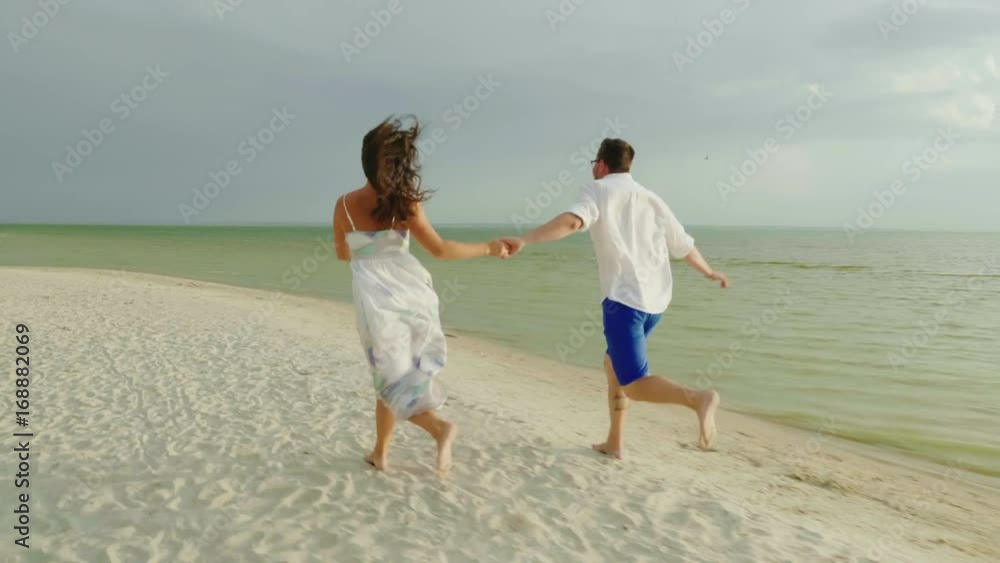 Young couple in love in light clothes carefree running on a clean tropical beach. 4K slow motion video Young couple in love in light clothes carefree running on a clean tropical beach. 4K slow motion video