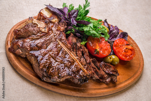 Appetizing steak on the bone, with tomatoes and herbs, on a wooden board. Horizontal frame photo