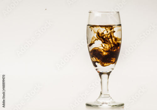 Dark brown food coloring diffuse in water inside wine glass with empty copyspace area for slogan or advertising text message, over isolated grey background. 