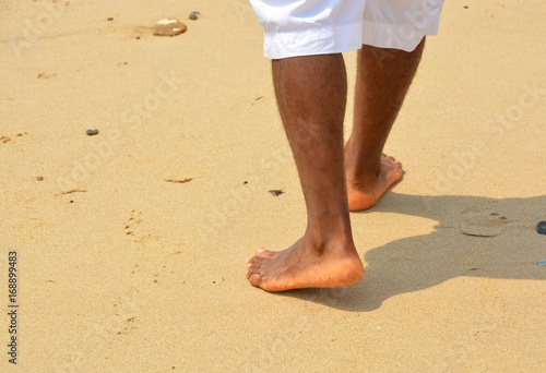 African american man walks on a sand beach. Close up of male feet and golden sand. Beach walk. Summer activity. Beautiful holiday background © Nataly Reinch