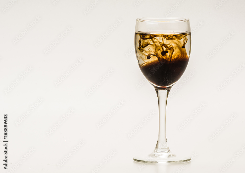 Dark brown food coloring diffuse in water inside wine glass with empty copyspace area for slogan or advertising text message, over isolated grey background. Dark brown food coloring diffuse in water inside wine glass with empty copyspace area for slogan or advertising text message, over isolated grey background.