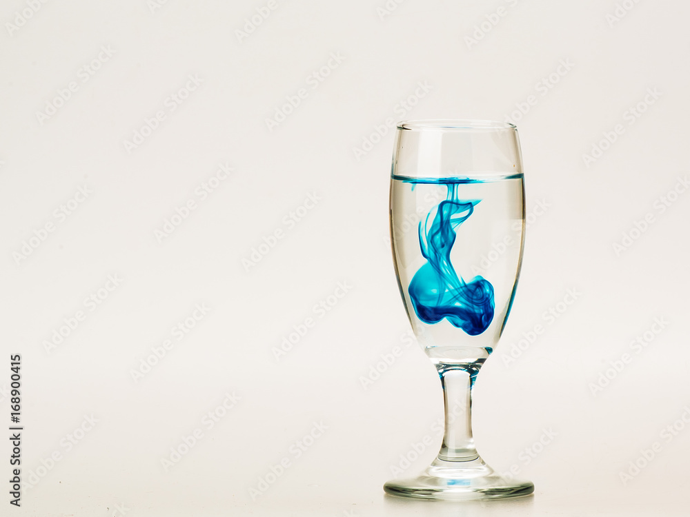 Blue food coloring diffuse in water inside wine glass with empty copyspace area for slogan or advertising text message, over isolated grey background. Blue food coloring diffuse in water inside wine glass with empty copyspace area for slogan or advertising text message, over isolated grey background.