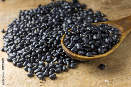 Sack of black beans spill beans with black beans in a wooden spoon on wooden table.