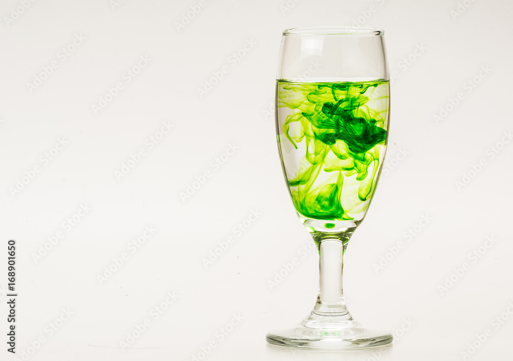 Green food coloring diffuse in water inside wine glass with empty copyspace area for slogan or advertising text message, over isolated grey background.
