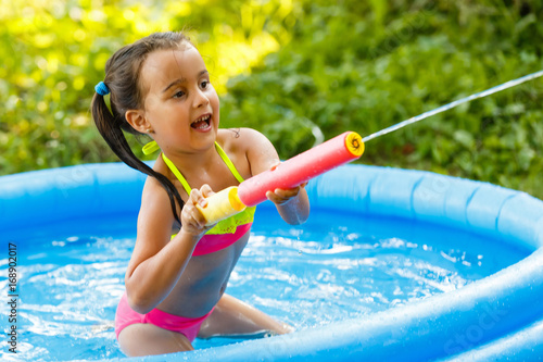 Photography A little girl is played by a water pump in an inflatable pool in the garden near