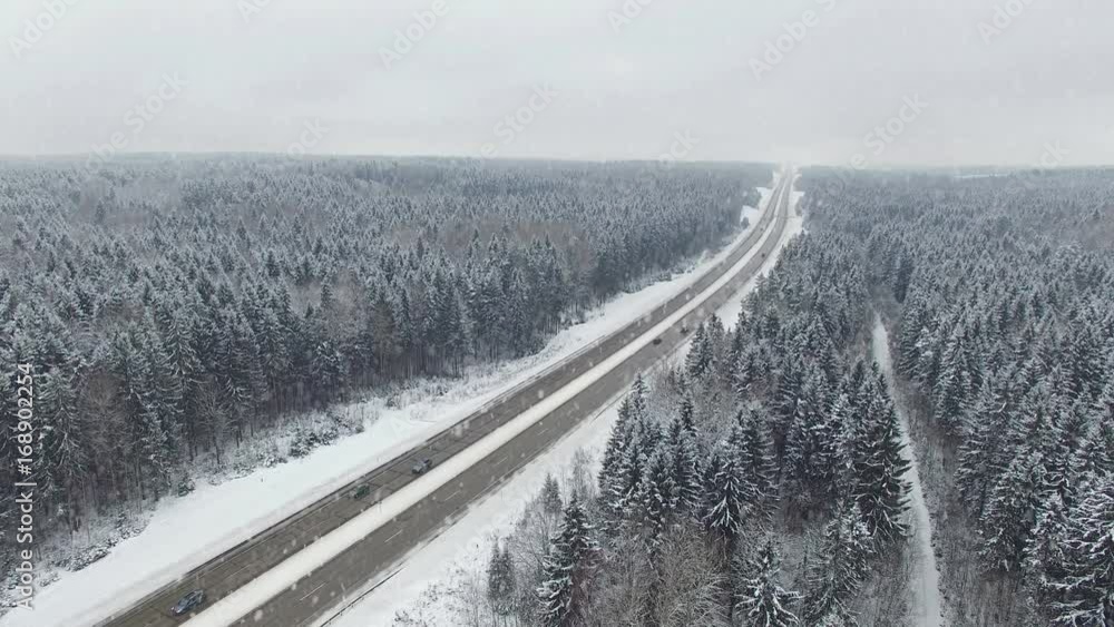 4K. Road in the winter forest with driving cars at snowfall. Aerial panoramic view. Vanishing point perspective. 4K. Road in the winter forest with driving cars at snowfall. Aerial panoramic view. Vanishing point perspective.
