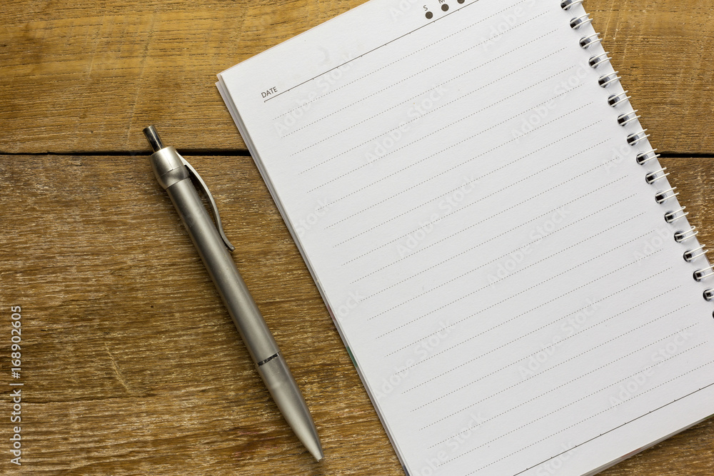 A blank notebook page and pen on wood office table. A blank notebook page and pen on wood office table.