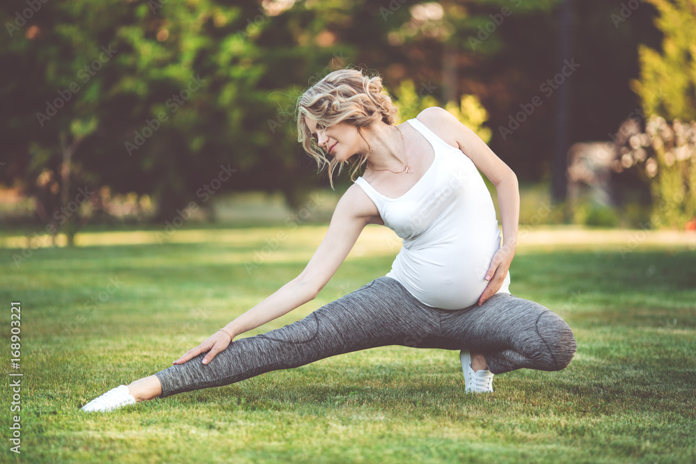 Beautiful slim sportive pregnant girl is doing sports on green grass
