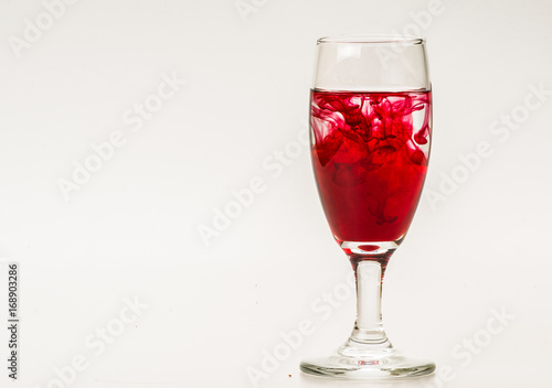 Red food coloring diffuse in water inside wine glass with empty copyspace area for slogan or advertising text message, over isolated grey background. 