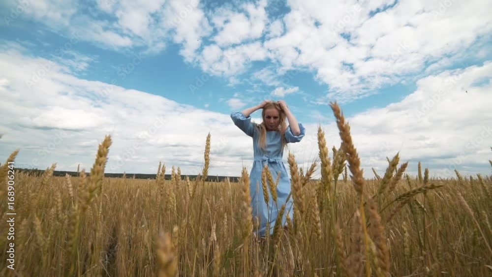 A young girl in a blue dress is standing in the field, and the wind is fluttering her hair A young girl in a blue dress is standing in the field, and the wind is fluttering her hair