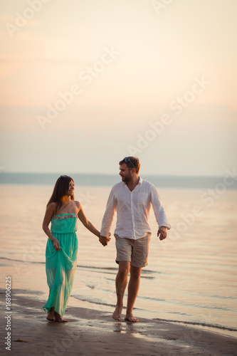 Enamored spouses hold each other's hands, a couple strolls along the beach in the evening, the sun goes over the horizon, the husband and wife take the day off together
