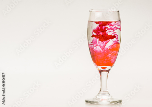 mixture of food coloring diffuse in water inside wine glass with empty copyspace area for slogan or advertising text message, over isolated grey background. 