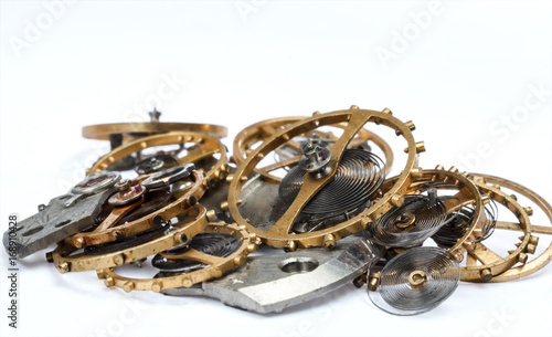 The details (gears, springs, pendulums) of the clockwork in a pile on a white background. Selective focus.